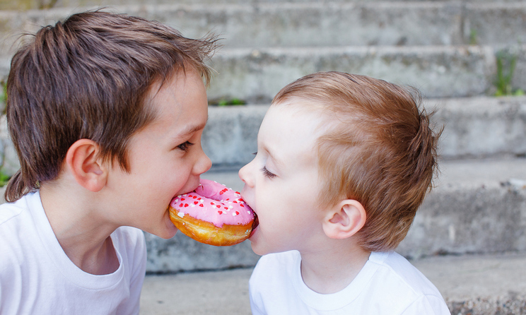 two kids bite off a donut and having fun